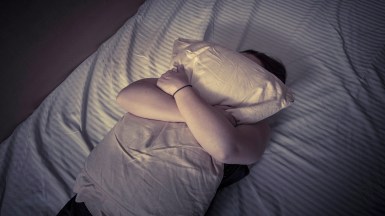 Image: Young woman lying in bed, clutching her pillow